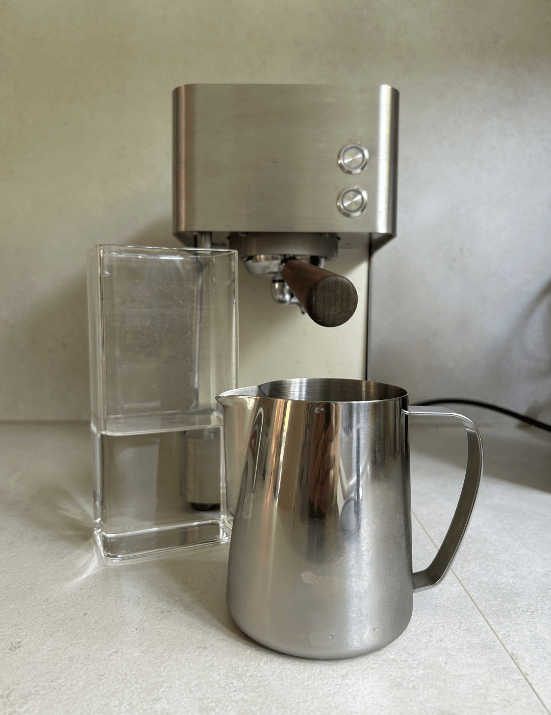 Mitgelieferter Wassertank aus Laborglas und größeres Milchkännchen im Größenvergleich vor der Zuriga E2-2