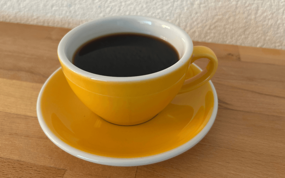 Schwarzer Kaffee ohne Milch in gelber Tasse mit Untertasse auf Holztisch