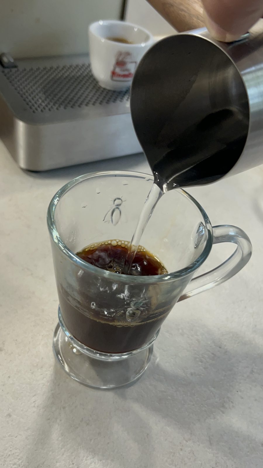 Einfacher Espresso im Glasbecher wird mit heißem Wasser zum Americano verlängert