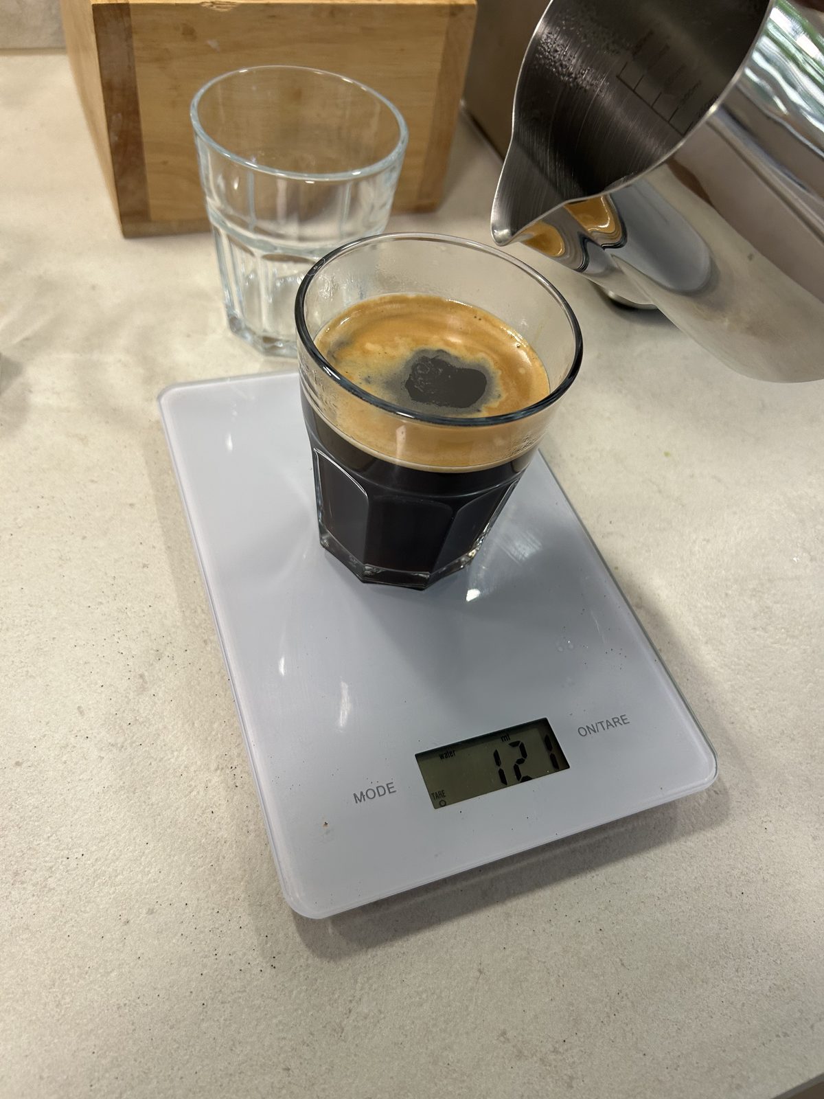 Heißes Wasser wird aus dem Milchkännchen auf einen Espresso mit Crema gegossen